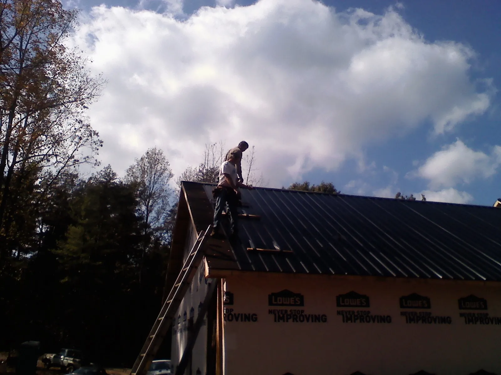 Roofer fastening dark metal panels high against a cloudy sky, from a Roof Inspection job in Everett